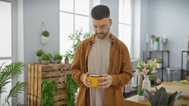 Sakallı İspanyol bir adam elinde parlak, bitki dolu bir çiçekçide kupa tutuyor..