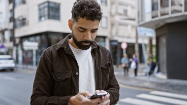 Meşgul şehir caddesinde akıllı telefon kullanan sakallı yakışıklı bir İspanyol..