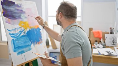 Parlak bir sanat stüdyosunda beyaz saçlı, esmer, olgun bir adam, yaratıcılık ve sanat eserlerini aktarıyor..