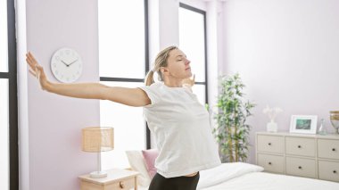 Genç sarışın bir kadın, modern bir dekorla parlak bir yatak odasında esniyor ve yeni bir sabahın habercisi oluyor..