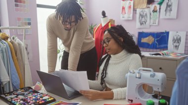 Kadın ve erkek, canlı bir terzi dükkanında dikiş aletleri arasında tasarımları inceleyerek iş birliği yapıyorlar..