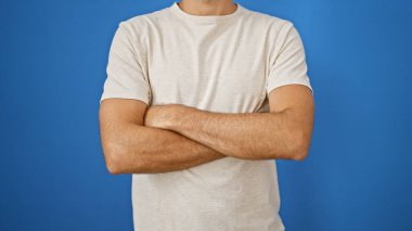 Kollarını kavuşturmuş sıradan, kendine güvenen İspanyol bir adam saf mavi bir arka plana karşı duruyor..