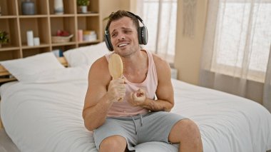 Genç İspanyol bir adam, kulaklık takıp, elinde saç fırçasını yatak odasında mikrofon olarak tutarak şarkı söylemekten hoşlanır..