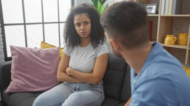Hoşnutsuz bir kadın ve bir erkek modern bir oturma odasında sohbet ediyorlar, ilişki dinamiklerini vurguluyorlar..