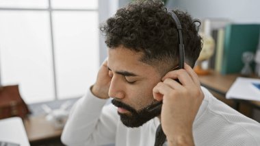 Sakallı, kulaklık takan ve modern bir ofiste çalışan düşünceli, genç bir İspanyol..