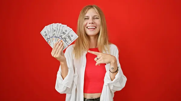 stock image Smiling young blonde woman holding money against a red background, portraying wealth and happiness.