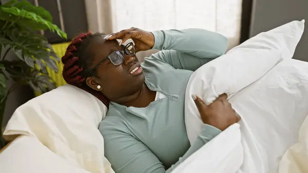 stock image An adult african american woman with braids experiences a headache while resting on a pillow indoors