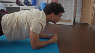 Genç İspanyol adam spor salonunda mavi paspas üzerinde tahta egzersizi yapıyor..