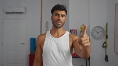 Spor aletleri, madalyalar, saat ve klimayla bir spor salonunda beyaz atlet giyen genç bir adam.