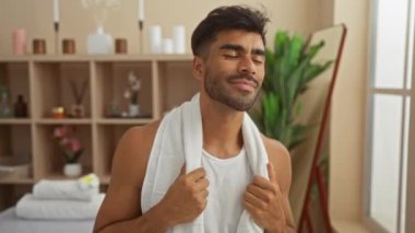 Genç bir adam sağlık salonunda spa tedavisinden zevk alıyor. İçi bambu bitkileri ve aynayla dolu. Omuzlarında havluyla yakışıklı ve rahat görünüyor.