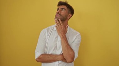 Beyaz gömlekli yakışıklı İspanyol bir adam parlak sarı bir arka plana karşı düşünceli bir şekilde poz verir..