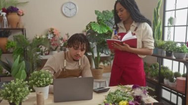 Çiçekçi dükkanında çalışan erkek ve kadın çiçekçiler, bitkiler, dizüstü bilgisayarlar ve not defterleriyle.