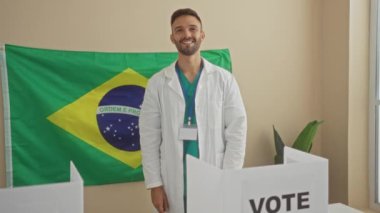 Beyaz önlüklü genç İspanyol bir adam. Kapalı bir Brezilya seçim odasında bayrak ve oy sancağıyla duruyor..