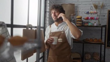Fırında kahve fincanı tutan genç adam konuşuyor. Etrafı taze hamur işleri ve ekmekle çevrili.