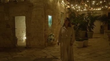 Genç İspanyol bir kadın polignano 'nun büyüleyici gece sokaklarında yürüyor. Bir kısrak, puglia, İtalya, aydınlık dekorasyonlar ve kırsal taş duvarlarla çevrili..