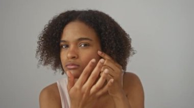 Kıvırcık saçlı Afrikalı Amerikalı genç bir kadın izole edilmiş beyaz arka plan duvarına sivilce çıkarıyor..