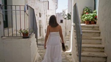 Beyaz elbiseli genç bir İspanyol kadın güneşli bir günde beyaz boyalı eski Ostuni, Puglia, İtalya 'da yürüyor..