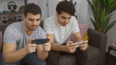 Modern bir oturma odasında akıllı telefonlarda video oyunu oynayan iki adam, boş zamanlarını ve teknolojiyi canlandırıyorlar..