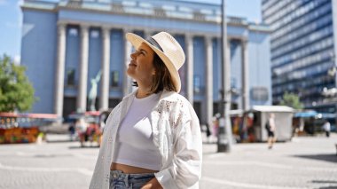 Güzel, genç, İspanyol bir kadın Nobel ödüllü bir binada yaz şapkası takmış, kendinden emin bir şekilde gülümsüyor.