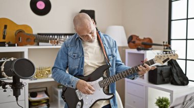 Evde müzik aletleri ve kayıt cihazlarıyla elektro gitar çalan olgun bir adam..