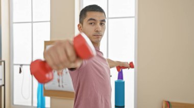 Işıl ışıl yanan bir rehabilitasyon kliniğinde dambıllarla egzersiz yapan genç bir İspanyol..