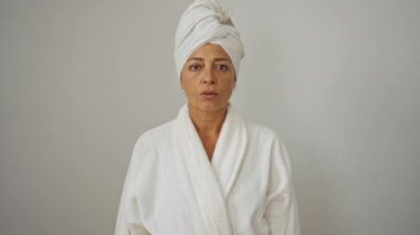 Bornoz ve havlu giymiş bir kadın, orta yaşlı, yüzünde şok ve şaşkınlık ifadesi, beyaz arka planda soyutlanmış, bornoz ve havlu giymiş, şaşkınlık ve korku gösteren bir kadın.