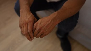 Elleri kelepçeli genç Afro-Amerikalı adam rahat bir evin içinde ahşap zeminli bir odada oturuyor.