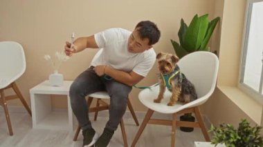 Genç adam, köpeğiyle veteriner kliniğinin bekleme odasında selfie çekiyor. Modern iç tasarımla dostane ve rahat bir atmosfer sergiliyor..