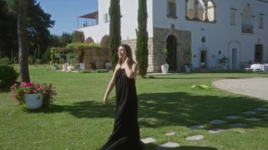 Siyah elbiseli genç bir İspanyol kadın Puglia, İtalya 'da yemyeşil, çiçekler ve manzaralı bir Akdeniz manzaralı bir bahçede güneşli bir günün tadını çıkarıyor..