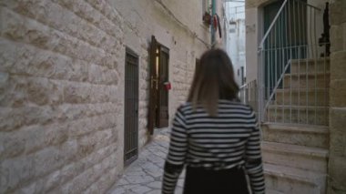 Genç bir İspanyol kadın polignano 'nun büyüleyici dar sokaklarında yürüyor taş binalarla çevrili Puglia, İtalya' da bir kısrak ve dokuma bir çanta taşıyor..