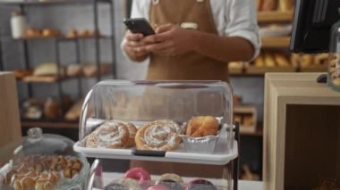 Pastanedeki genç adam tezgahında hamur işleri olan akıllı bir telefon kullanıyor.