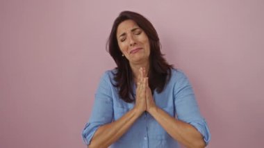 Minnettarlığını ifade eden neşeli bir kadın, elleri bağlı, mavi bir gömlek giymiş, izole edilmiş pembe bir arka plan duvarına yaslanmış..