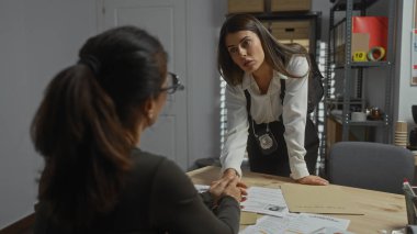 Kadın dedektif şüpheliyi polis merkezinde sorguluyor. Belgeler ve rozetler ortada..