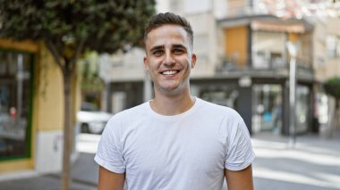 Yakışıklı, genç, İspanyol bir adam güneşli bir şehir sokağında güvenle gülümsüyor..
