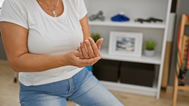 Orta yaşlı bir kadın evde bilek egzersizi yapıyor. Belki bir rehabilitasyon merkezinde..