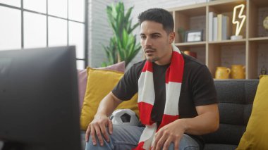 Sakallı genç bir İspanyol adam rahatlık ve rahatlığı ima ederek rahat bir oturma odasında televizyon izliyor..