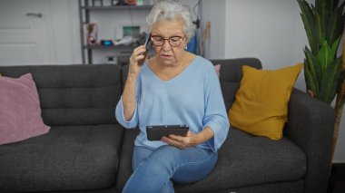 Üst düzey kadın oturma odasında akıllı telefon kullanıyor ve tablet okuyor..