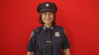 Üniformalı, gülümseyen orta yaşlı İspanyol bir kadın polis, izole edilmiş bir kırmızı arka plana karşı duruyor..