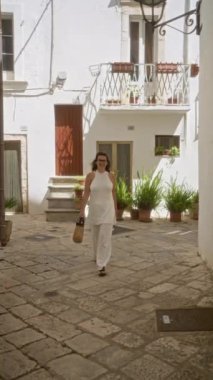 Genç bir İspanyol kadın, beyaz binalar ve saksı bitkileriyle çevrili İtalya 'nın eski bir kasabasında Locorotondo, Puglia' nın büyüleyici, kaldırım taşı sokaklarında geziniyor..