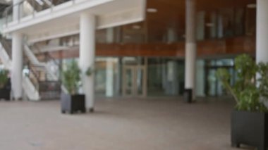 Beyaz sütunlar ve cam kapıların yer aldığı doğal ışıklandırması olan modern bir ofis lobisinin bulanık görüntüsü.