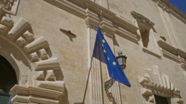 Avrupa Birliği bayrağı güneşli bir günde Güney İtalya 'da Lecce, Puglia' daki tarihi bej taş binasının önünde dalgalanıyor.