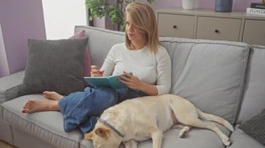 Düşünceli bir kadın, dinlenme köpeğinin yanındaki defterine rahat bir oturma odasındaki kanepede yazıyor.