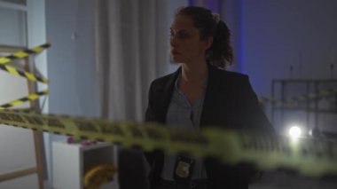 Odaklanmış genç bir kadın dedektif ön planda dikkat bandıyla kapalı bir suç mahallini inceliyor..