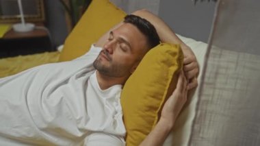 Yakışıklı, genç, İspanyol bir adam evindeki sarı yastığının üzerinde rahatlıyor. İçerideki rahat ortamda sakinlik ve memnuniyet yayıyor..