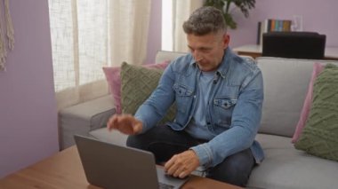 Oturma odasındaki koltukta oturan orta yaşlı bir adam içeride dizüstü bilgisayarla etkileşime geçiyor.