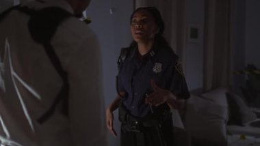 Polis kadın ve erkek, kırmızı ve mavi ışıklandırmalı bir olay yerinde kapalı alanda bir davayı tartışıyorlar.