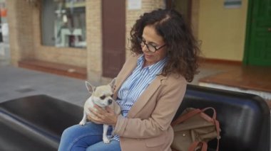 Bir kenar mahalledeki bankta otururken elinde chihuahua tutan orta yaşlı bir kadın..