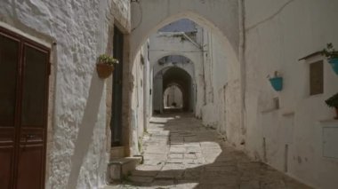 Ostuni, puglia, İtalya 'daki pitoresk dar bir sokakta beyazlatılmış taş duvarlar, dekoratif bitkiler, kemerler ve kaldırımlar yer alıyor..