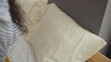 Evde, yatak odasında, sarı battaniyeli çizgili pijama giymiş bir kadın içeride huzurlu bir an sergiliyor.