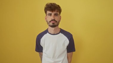Genç, İspanyol bir adam utandı, yüzünde negatif bir ifade ile korku içinde durdu. El, göz kapaklarını kapadı. İzole edilmiş sarı arka plan kavramının üzerine.